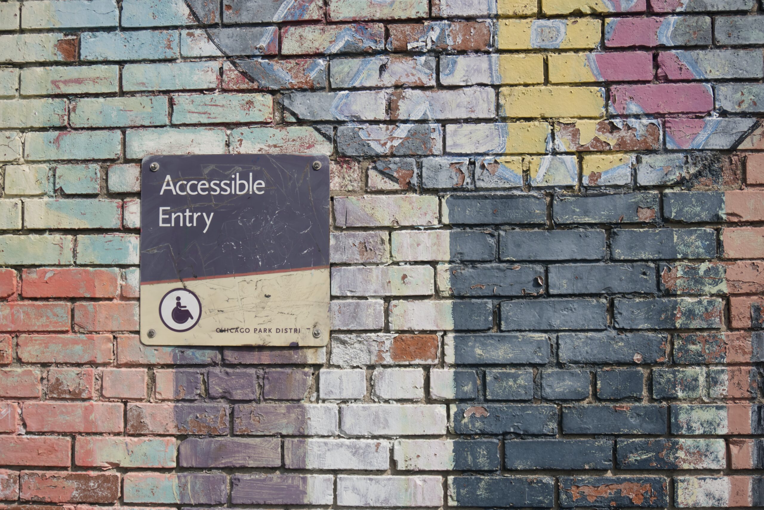 Brick wall with graffiti next to sign that reads "Accessible entry" with a small wheelchair symbol. The sign is from the Chicago Parks District.